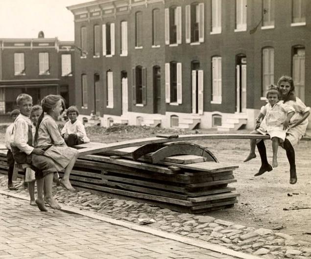 Children improvise a dangerous seesaw from construction materials on an unpaved road in Baltimore, 1914.